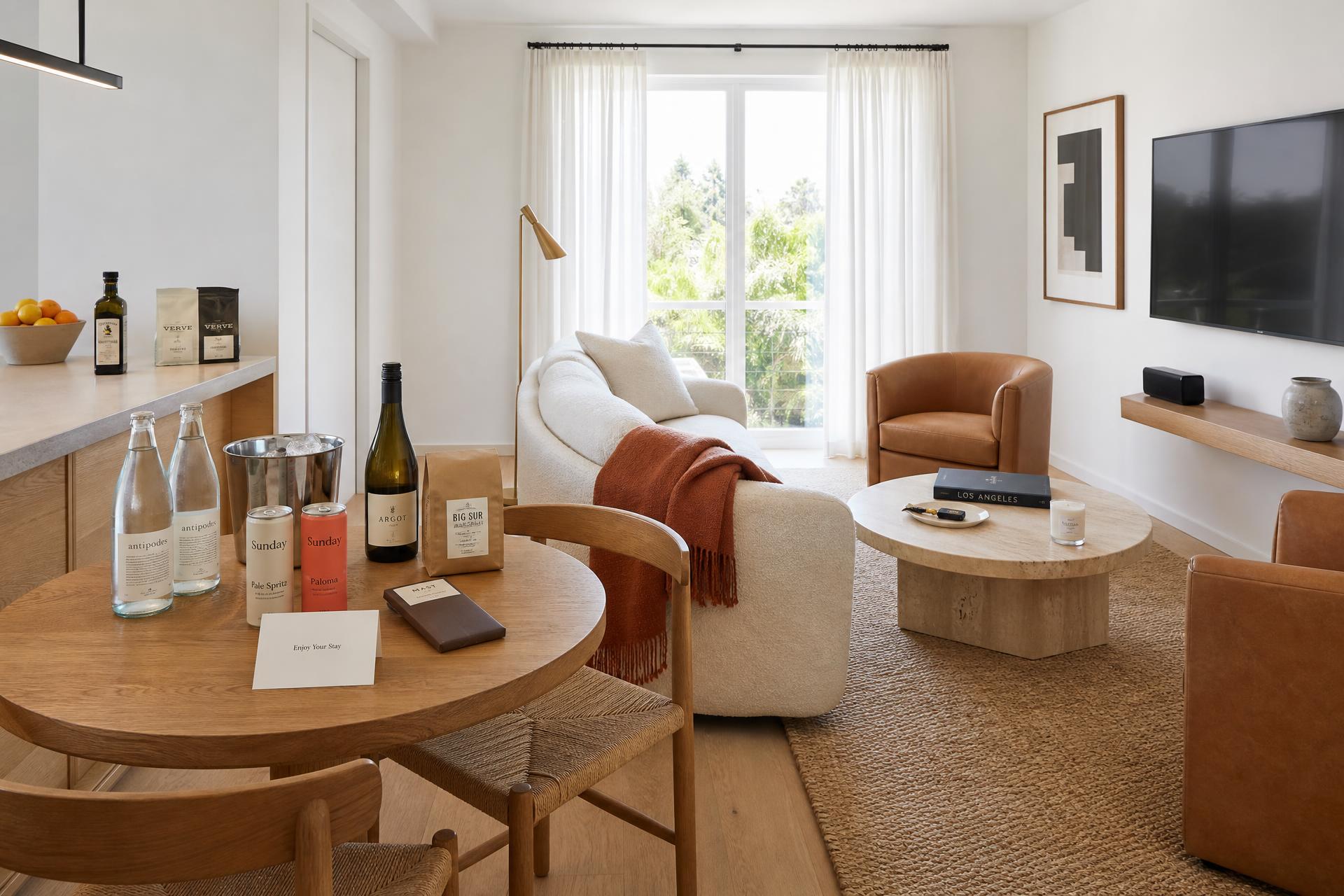 Open-plan living room with dining table, boucle sofa, leather chair, and media wall